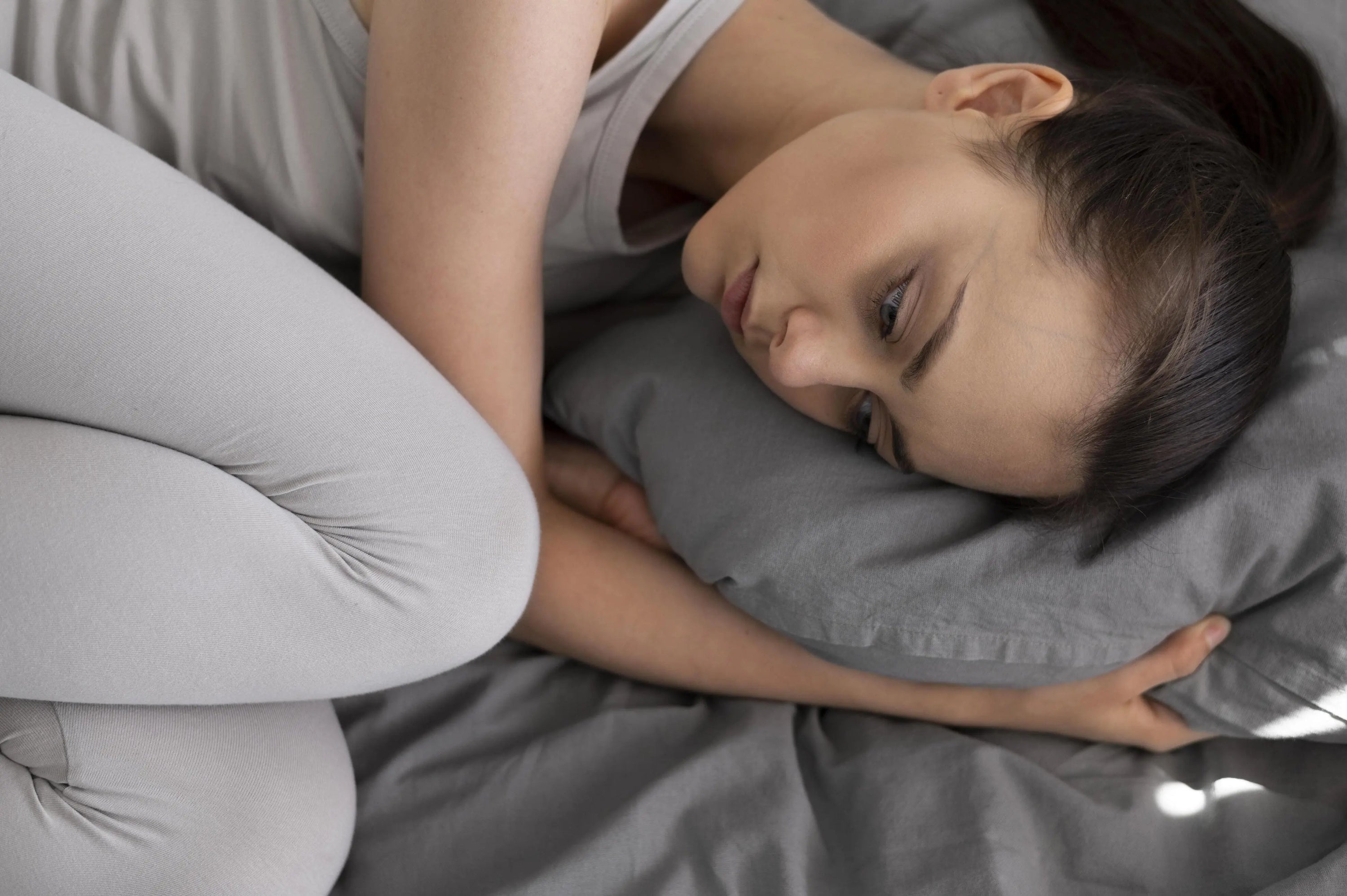 Young woman lying in bed struggling to fall asleep, looking restless and uncomfortable.