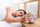 A tired young woman lying in bed, reaching for her alarm clock before it rings, in a softly lit bedroom.