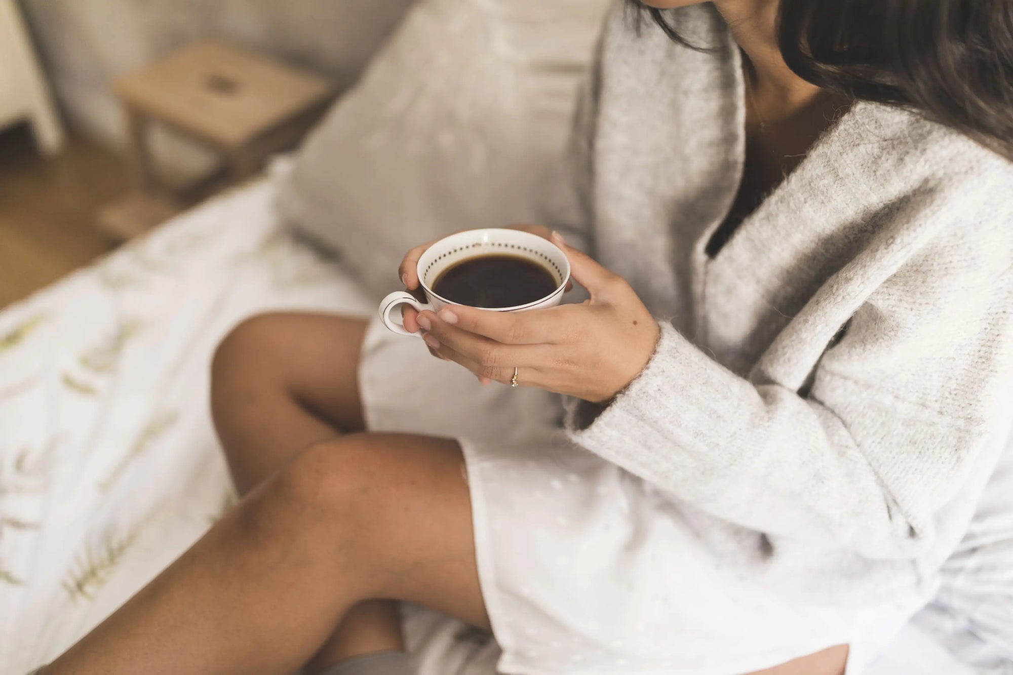 Top view of a young woman sitting on a bed holding a cup of coffee, highlighting the link between caffeine and sleep quality.