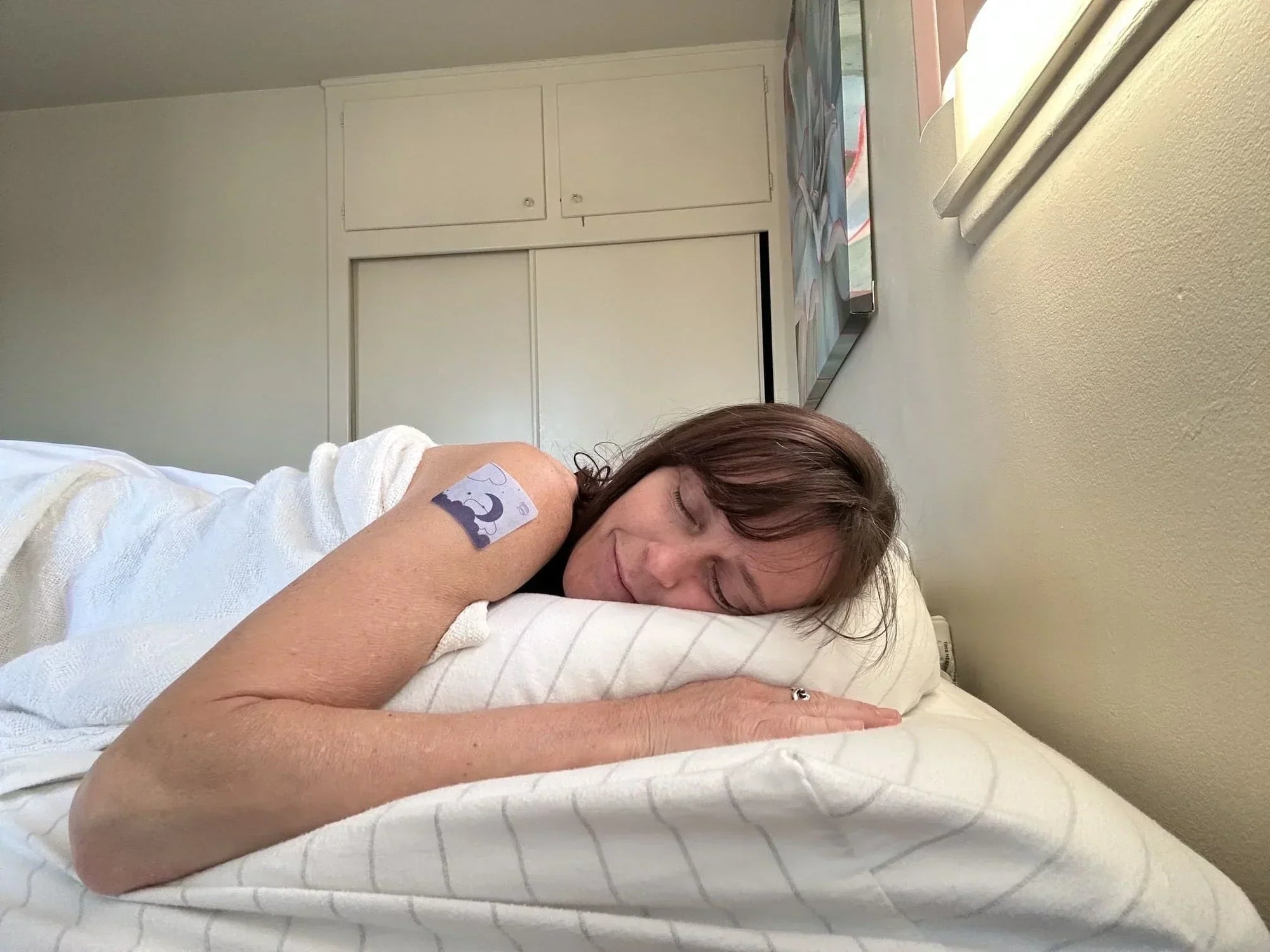 Woman sleeping peacefully with Vitalisys Sleep Patch on upper arm in natural bedroom light