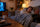 Woman in her 50s asleep on the sofa under a blanket in the evening with the TV on and a warm lamp in the living room"
