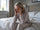 Woman in her 50s sitting on the edge of the bed in the morning holding her head, looking tired despite a full night's sleep